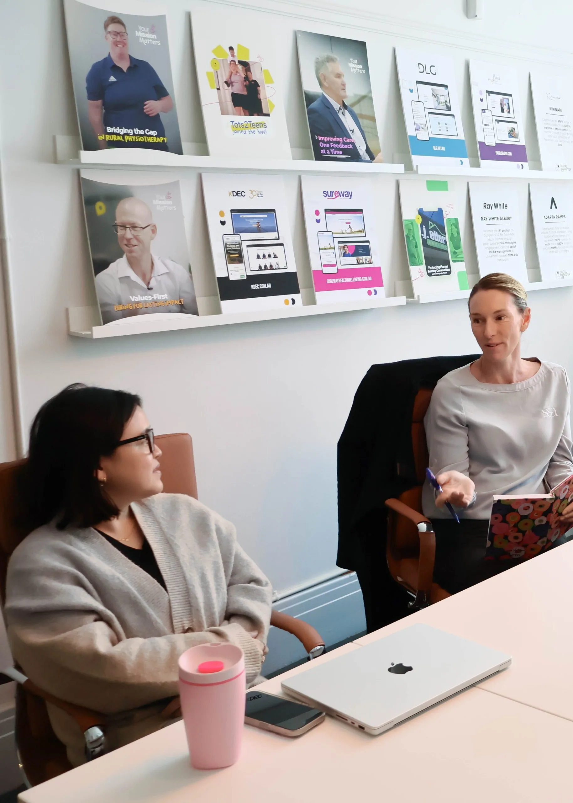Digital Marketer Bee team collaborating in a client strategy session, with marketing portfolio work displayed on a wall shelf in the background